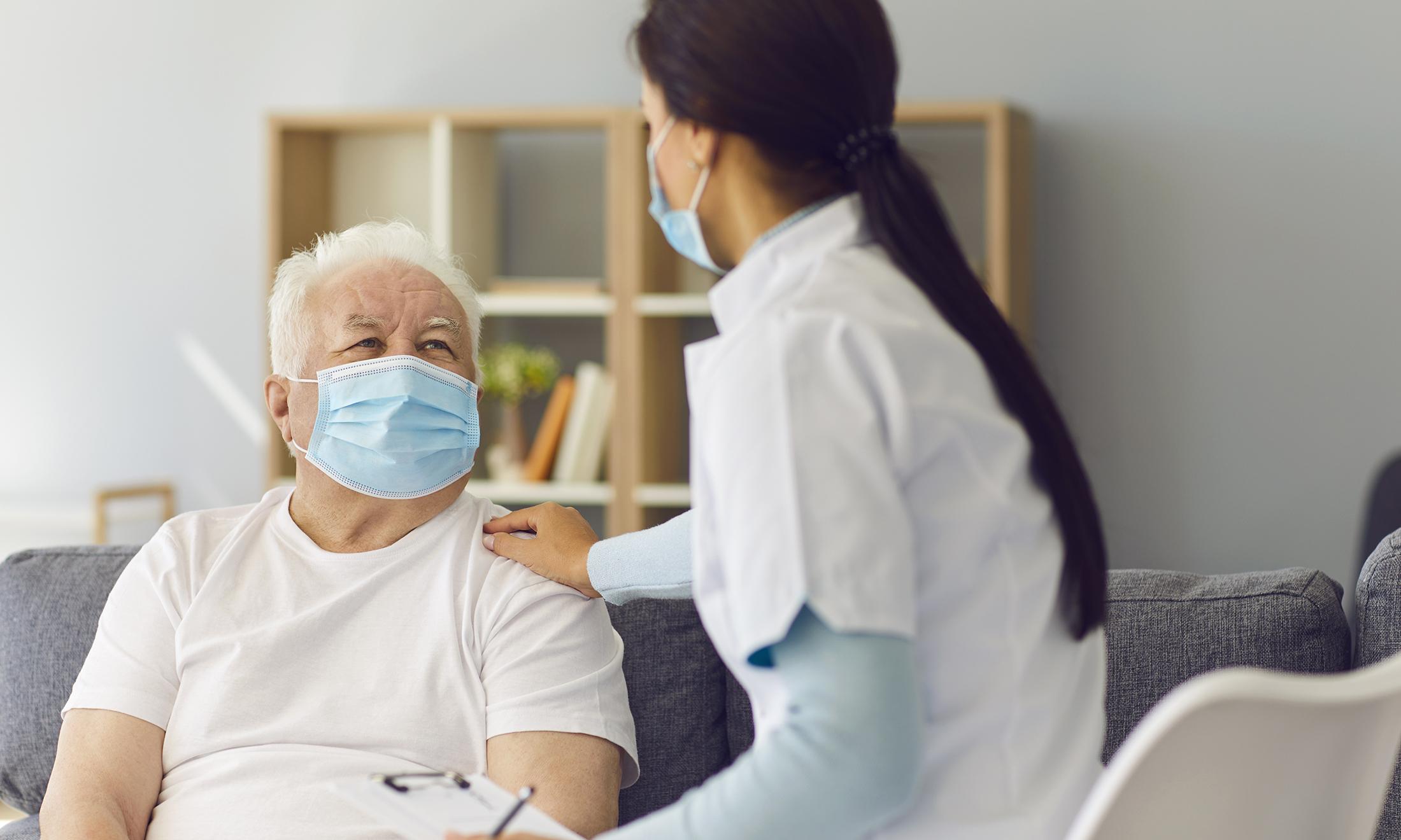 An image of a senior citizen wearing a mask and talking to a doctor